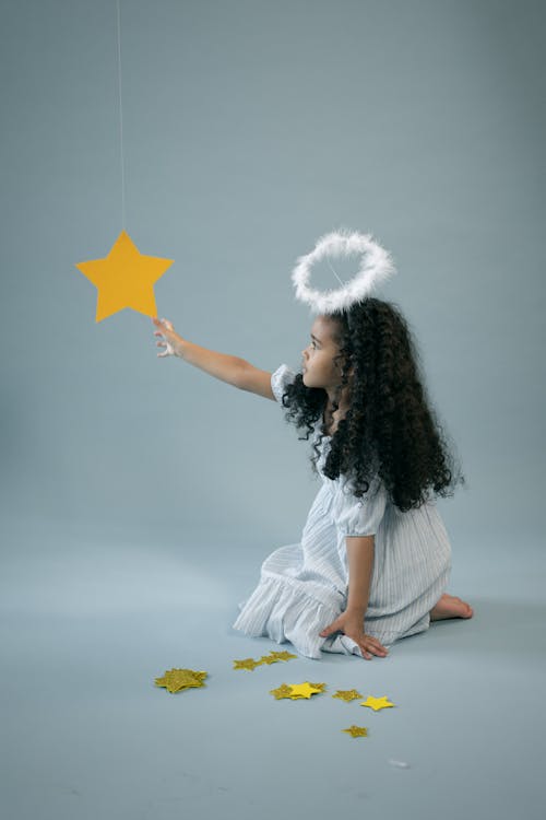 Free Cute black girl in angel costume showing star Stock Photo