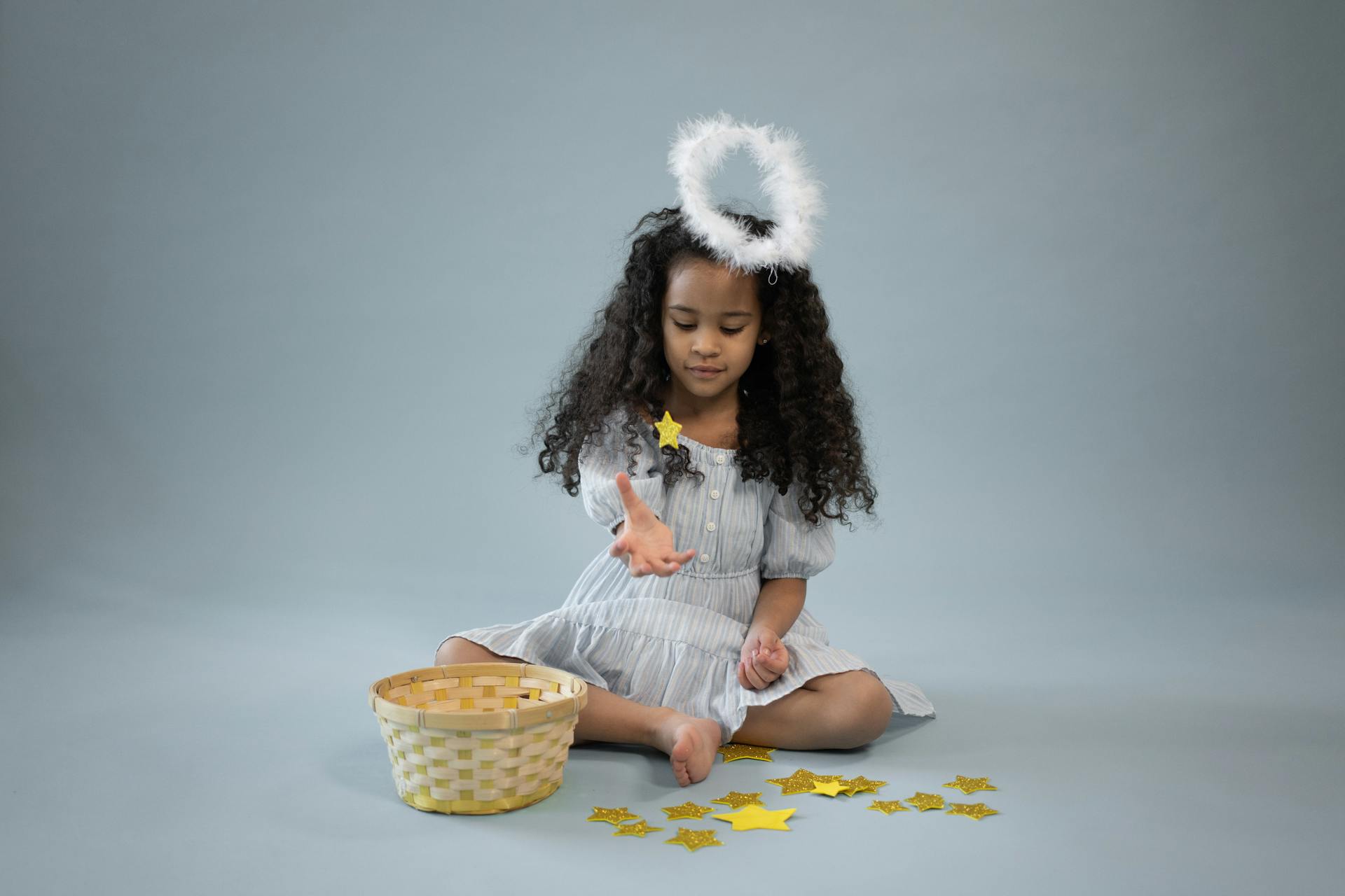 Content black girl in angel outfit playing with yellow stars