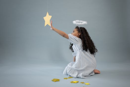 Black girl in angel outfit touching star