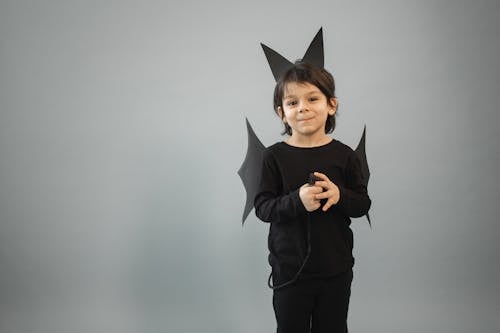 Free Positive boy in black bat outfit with wings and ears looking at camera on gray background with tail in hands Stock Photo