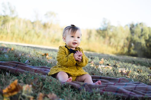 無料 茶色のテキスタイルに座っている黄色のかぎ針編みの長袖ドレスを着ている赤ちゃん 写真素材