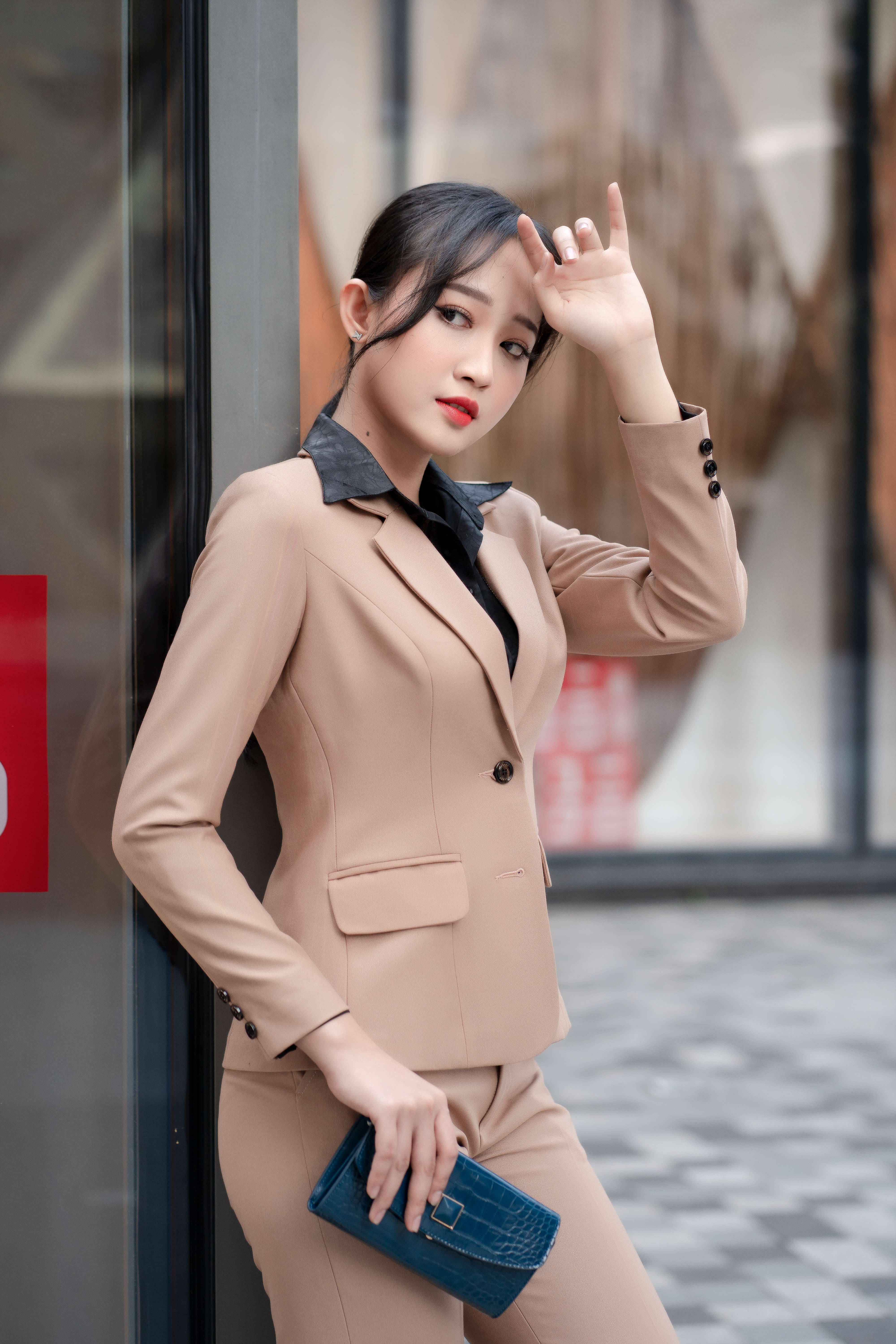 Asian woman in beige business suit with blue clutch, standing outdoors. Stylish and modern.