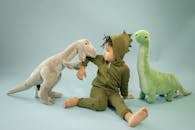 African American child with dreadlocks in dinosaur costume sitting between soft toys representing bite concept