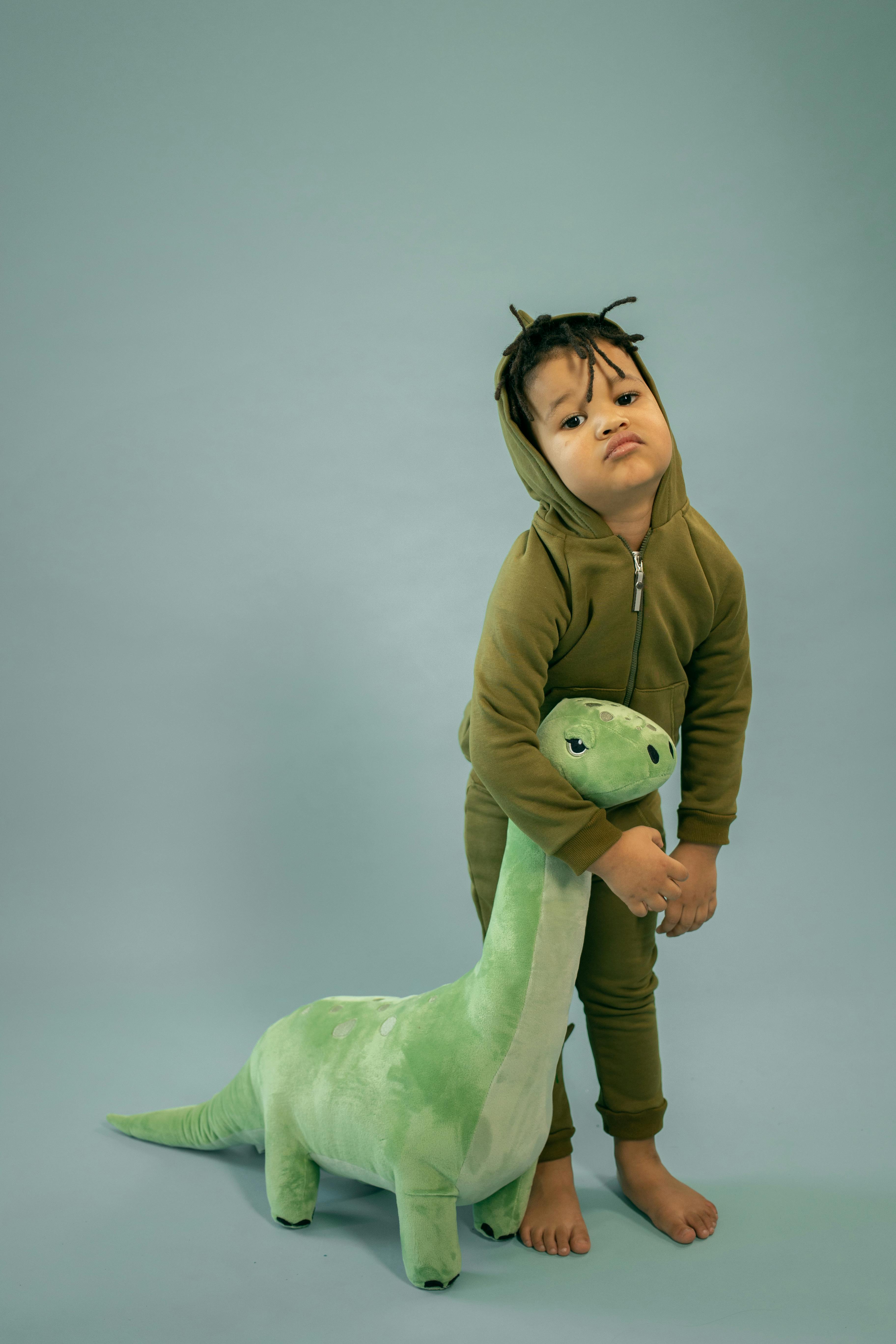 bored black boy embracing toy dinosaur on gray background