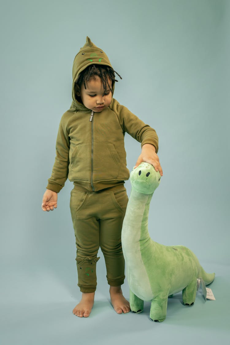 Ethnic Boy Caressing Toy Dinosaur On Gray Background