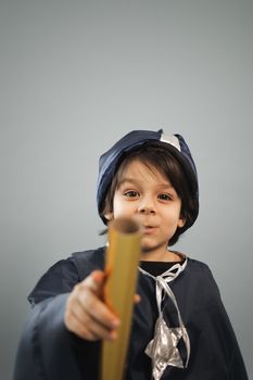 Young boy in a wizard costume holding a scroll, posing in a studio setting.