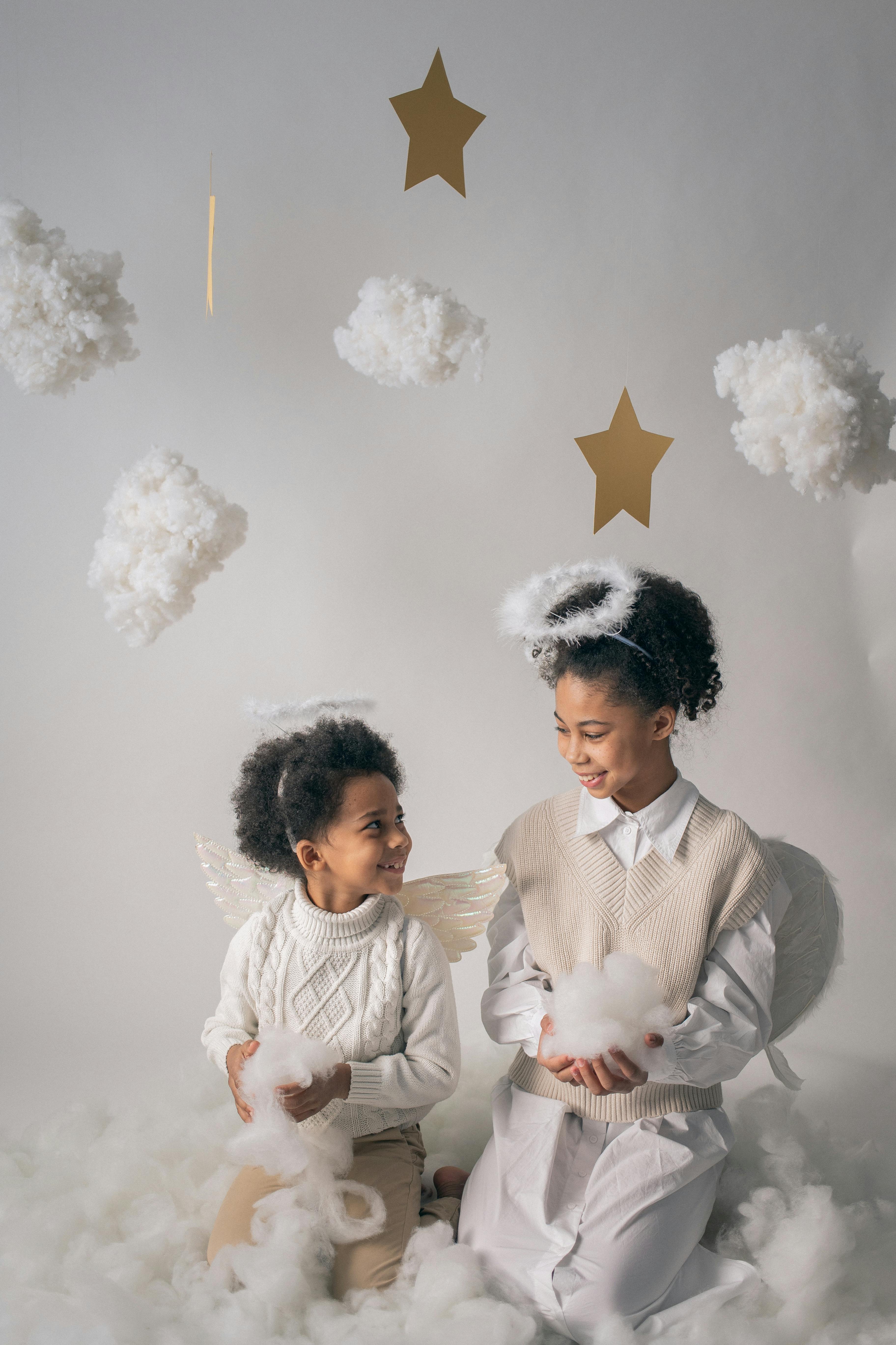 smiling black siblings in angel costumes under decorative clouds