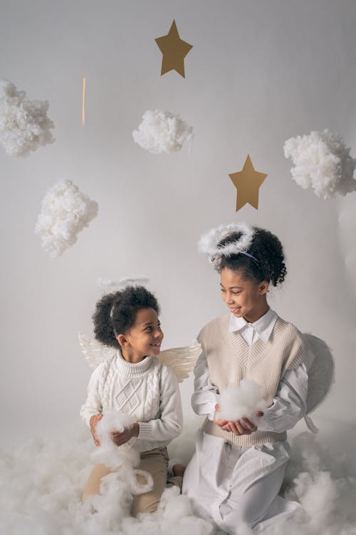 Smiling black siblings in angel costumes under decorative clouds