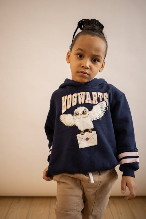 Confident African American kid with braids wearing hoodie and pants standing in studio and looking at camera