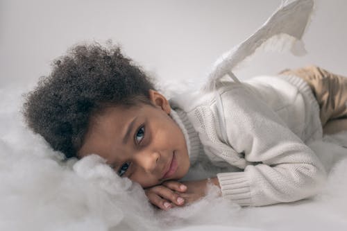 Cute black boy in angel costume lying on cotton cloud