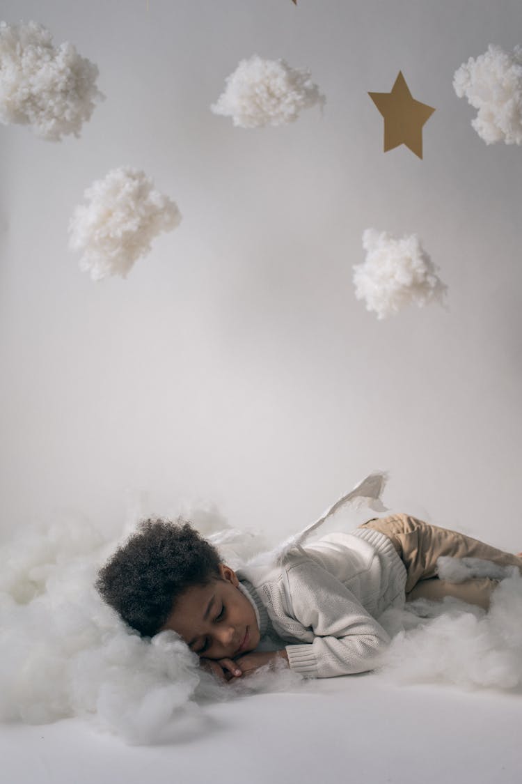 Sleepy Black Boy In Angel Costume Sleeping In Decorated Studio