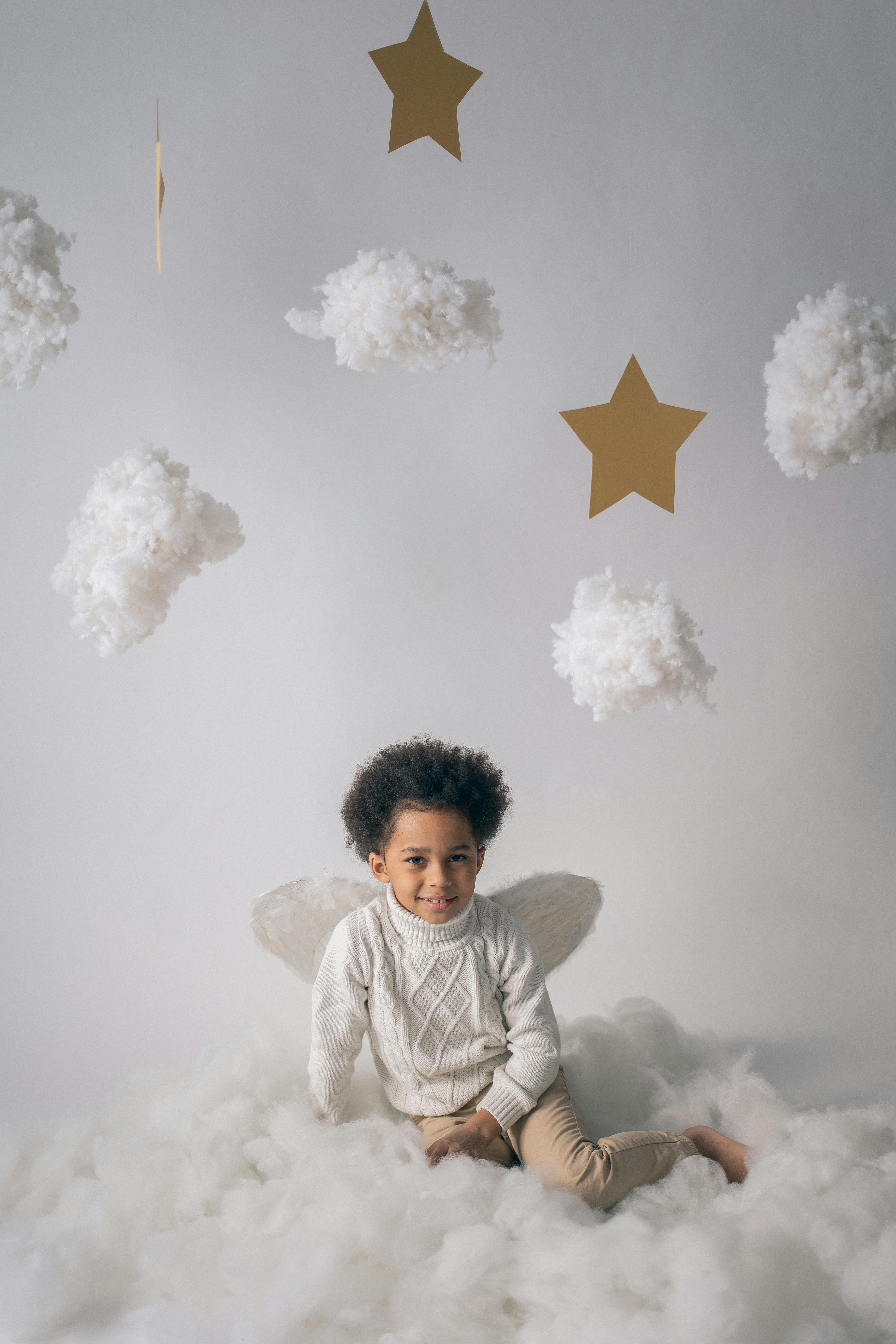 adorable black boy in angel wings near decorative clouds