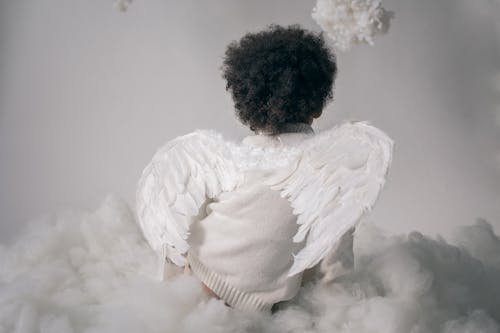 Anonymous boy in angel wings sitting on cotton cloud