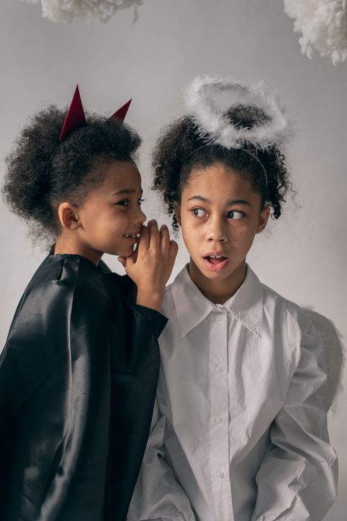 Free African American children in Halloween outfits of demon and angel looking away on white background in light studio Stock Photo