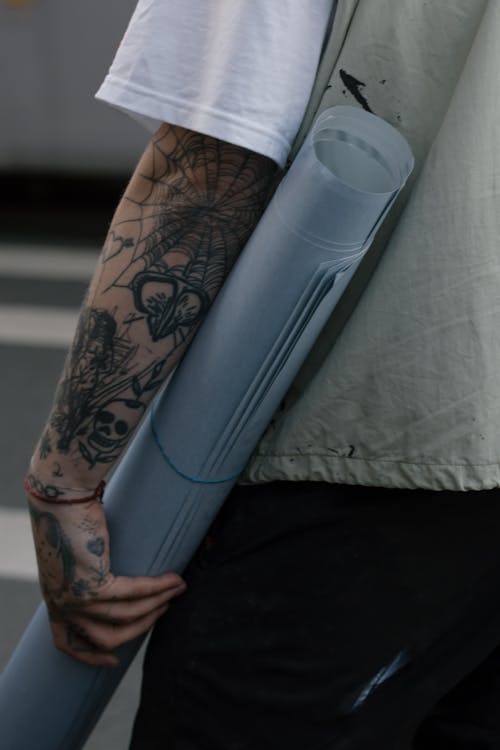 Free Person with Arm Tattoo Holding a Rolled Paper Stock Photo