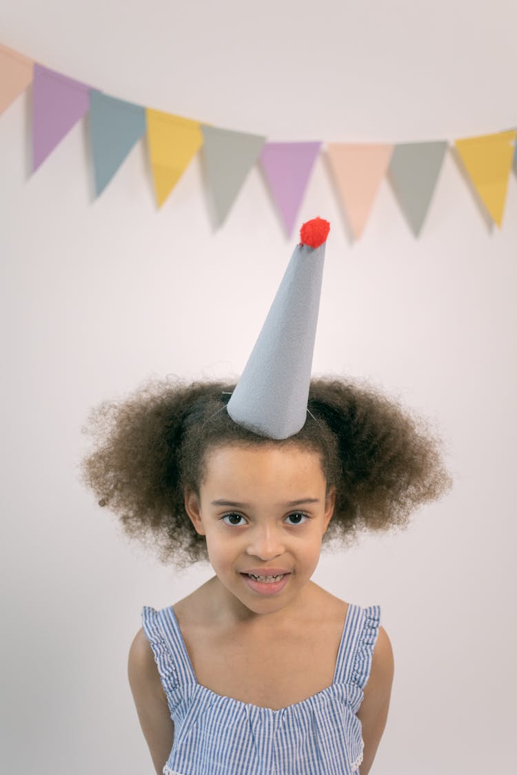 Happy Girl With Party Hat Standing Near Flag Garland