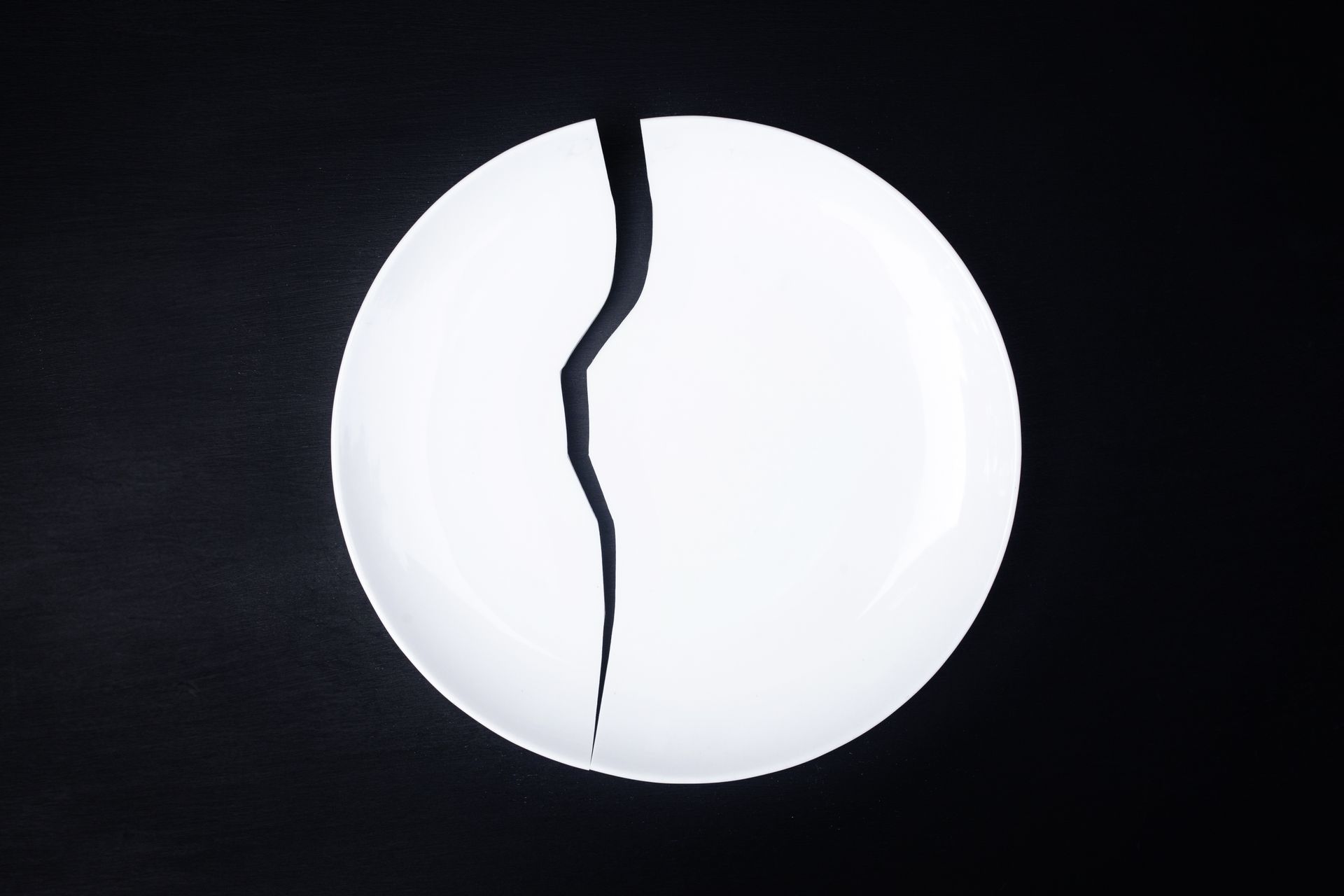 Top view of broken round shaped white porcelain plate with wavy crack on black background