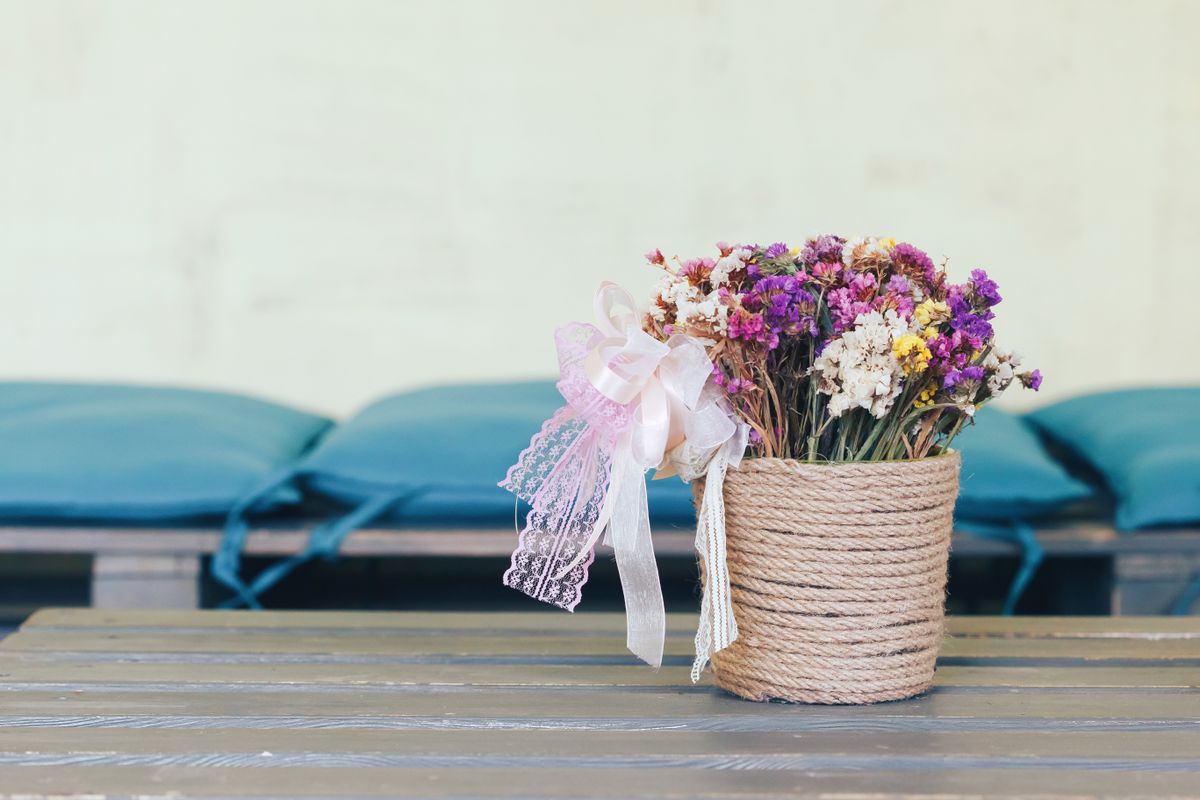 Clay pot craft ideas with a rope-wrapped pot holding dried flowers on a table