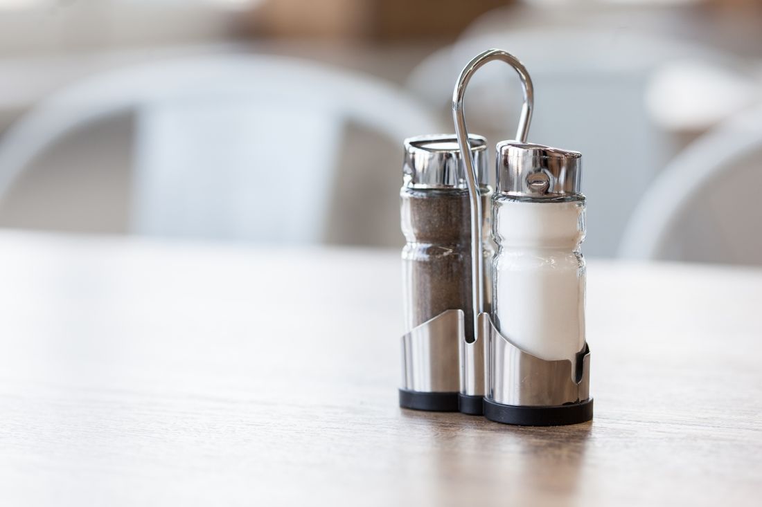 Glass salt and pepper shakers in a stainless steel caddy on table