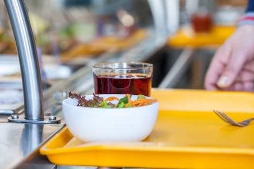 Free Crop unrecognizable person with bowl of delicious salad and glass of refreshing drink in self service restaurant Stock Photo