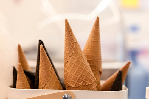 Crunchy tasty vanilla and chocolate waffle cones in container in workspace on blurred background