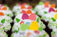 Small tasty desserts with bright decorative eggs and leaves in whipped meringue cream during Easter holiday