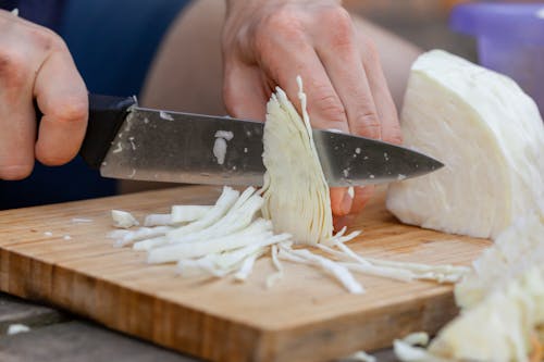 Crop anonymous male cook chopping ripe cabbage with sharp knife on timber board in kitchen