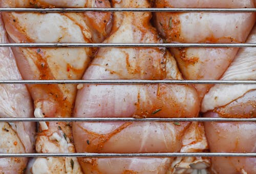 From above of closeup of raw chicken legs with seasoning cooking on metal grill grate