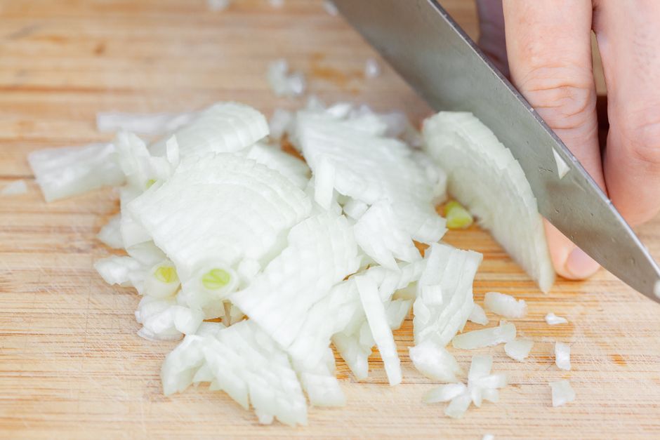 From above crop unrecognizable chef cutting fresh ripe onion on wooden cutting board in daylight