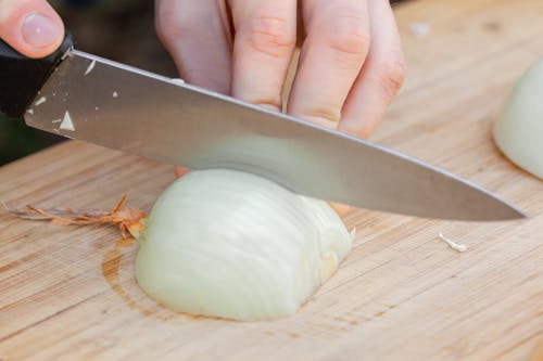 Person cutting onion on wooden cutting board