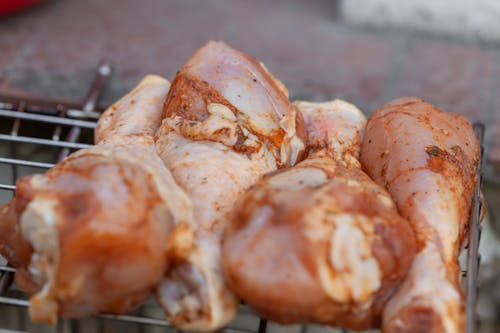 From above of raw chicken legs with seasoning placed on metal grill grate in daylight