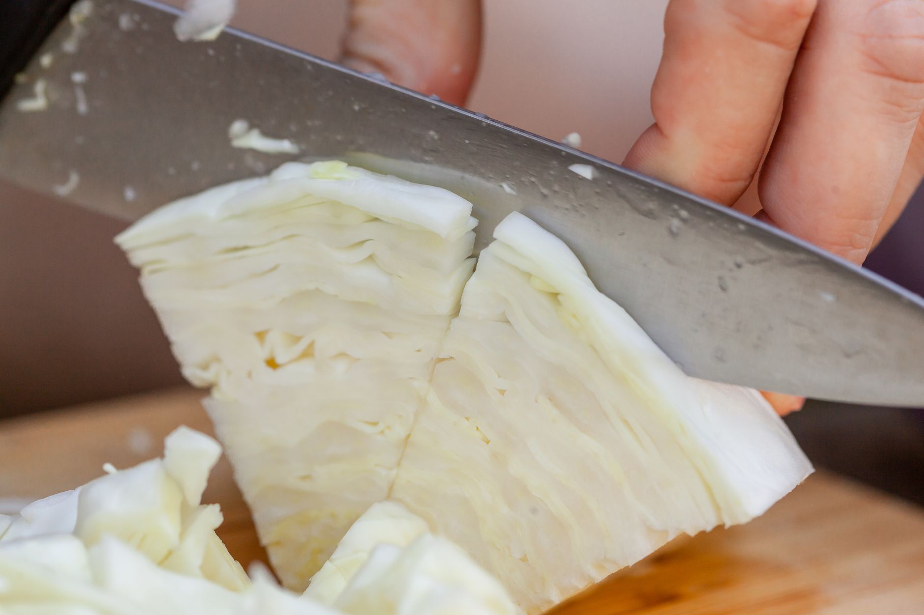 Crop unrecognizable cook cutting fresh ripe cabbage on wooden cutting board in daytime