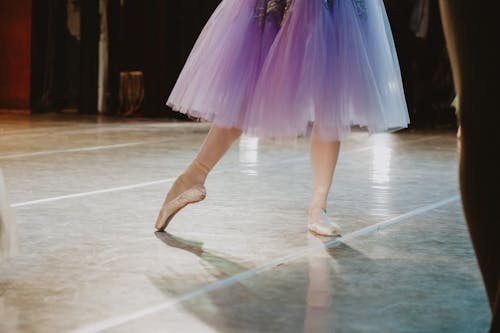 Crop anonymous female balerina in stylish tutu and pointe shoes dancing on stage during concert