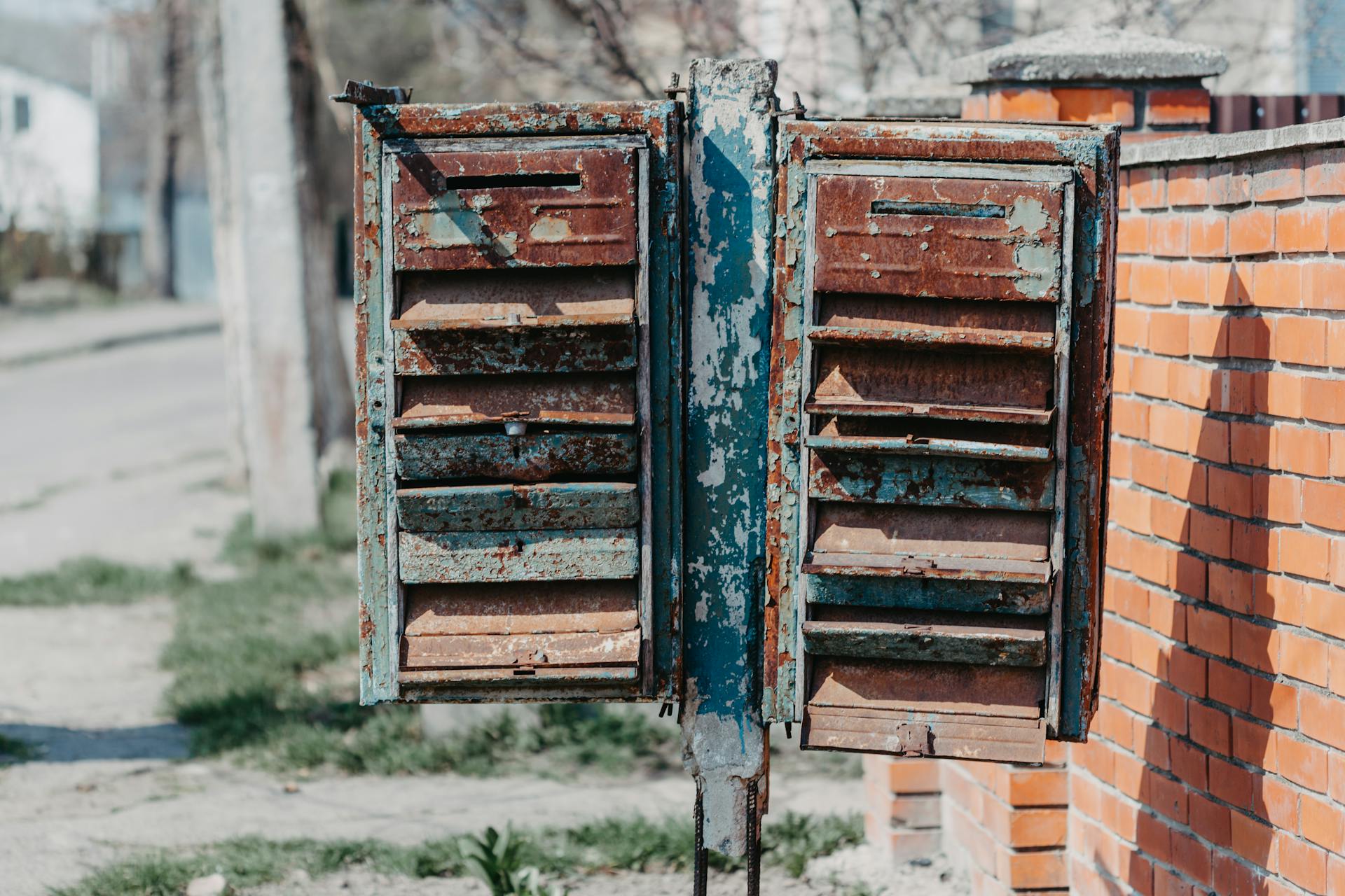 Aged rustic mailboxes placed near brick fence on street in town in sunny day