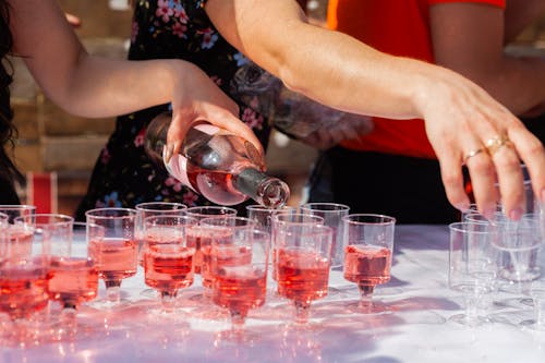 Crop anonymous female pouring red alcohol into transparent cups for guests at festive event