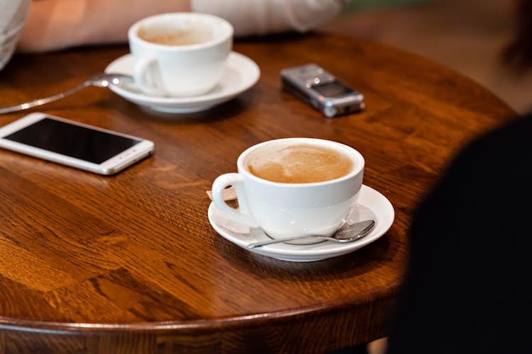 Coffee Cups On Saucer Near Smartphone And Voice Recorder On Table