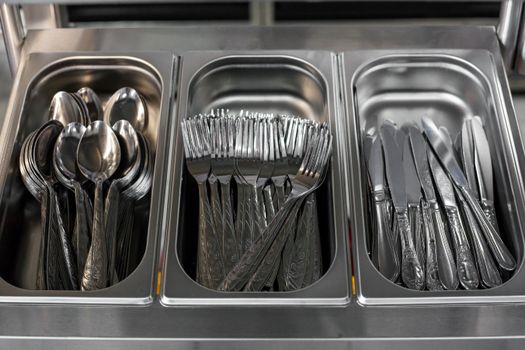 From above of metal knives forks and spoons placed in metal containers in canteen