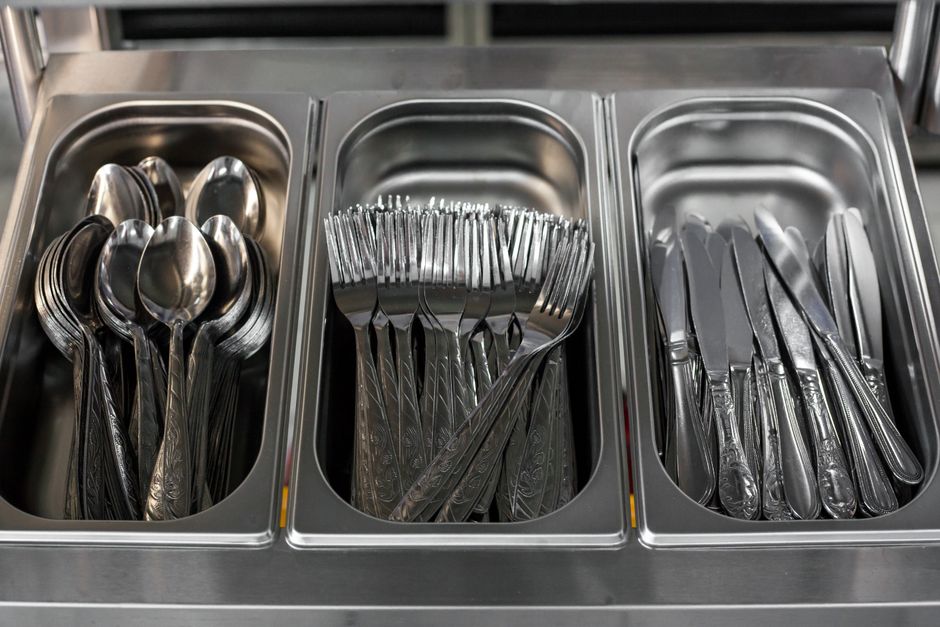 From above of metal knives forks and spoons placed in metal containers in canteen