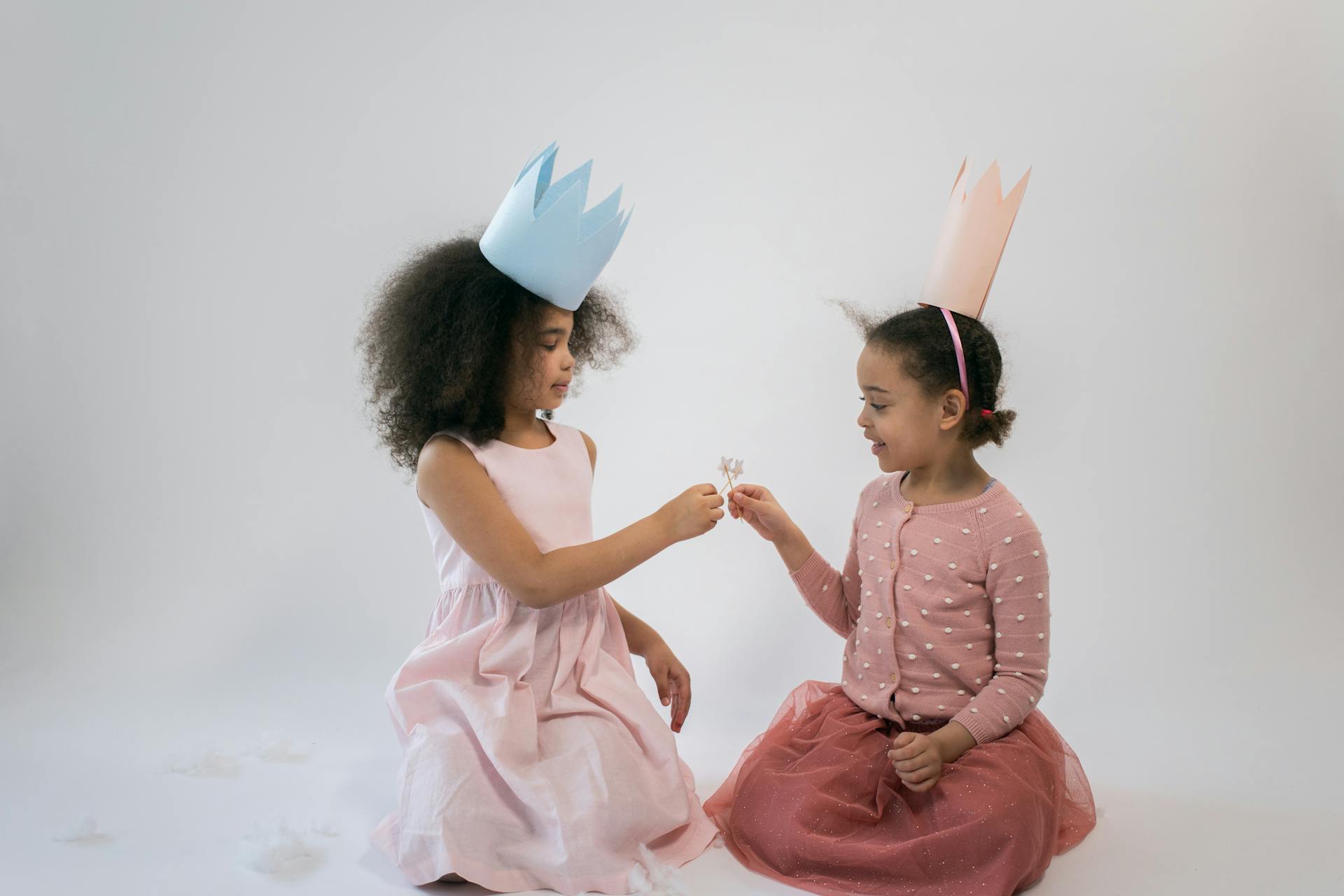 Two young girls in princess crowns enjoying a playful moment indoors on a white background.