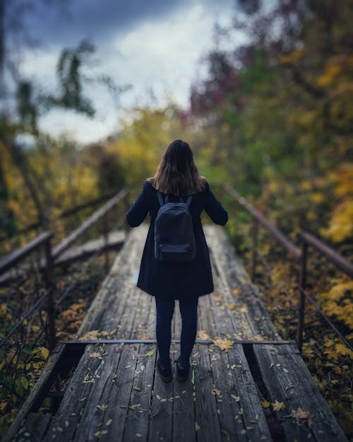 бесплатная Селективный фокус фотографии женщины в черном пальто, стоящей на деревянном мосту Стоковое фото