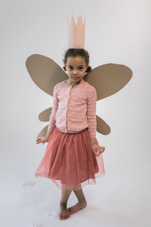 Cute black kid with paper crown and butterfly wings standing in white studio