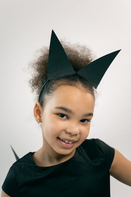 Positive little black child in carnival costume smiling at camera in studio