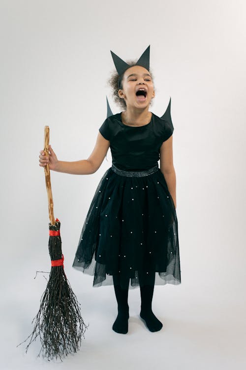 Cute little black girl in Halloween costume standing in studio with broom and screaming