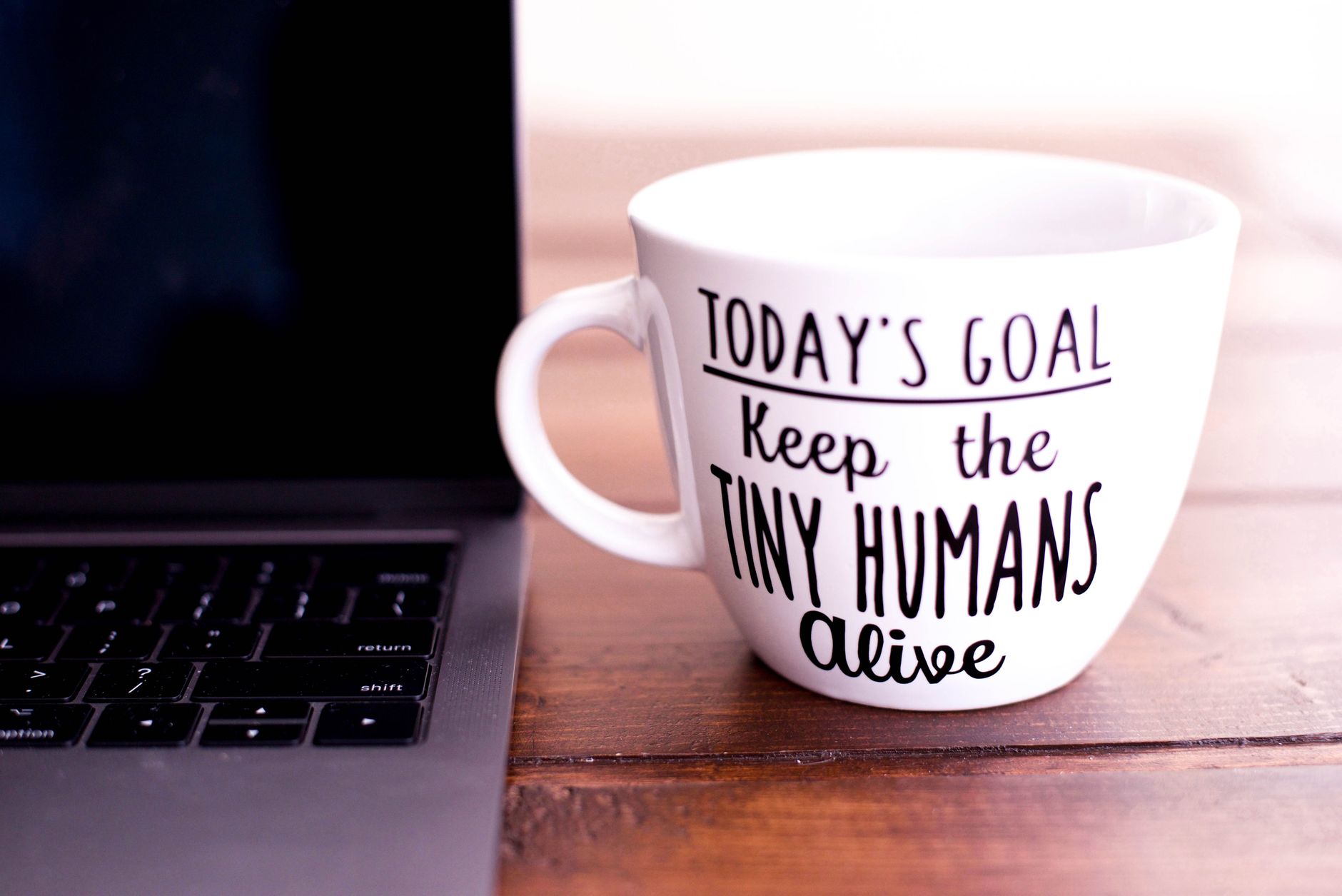 Close-up of a mug with motivational text beside a laptop on a wooden desk.