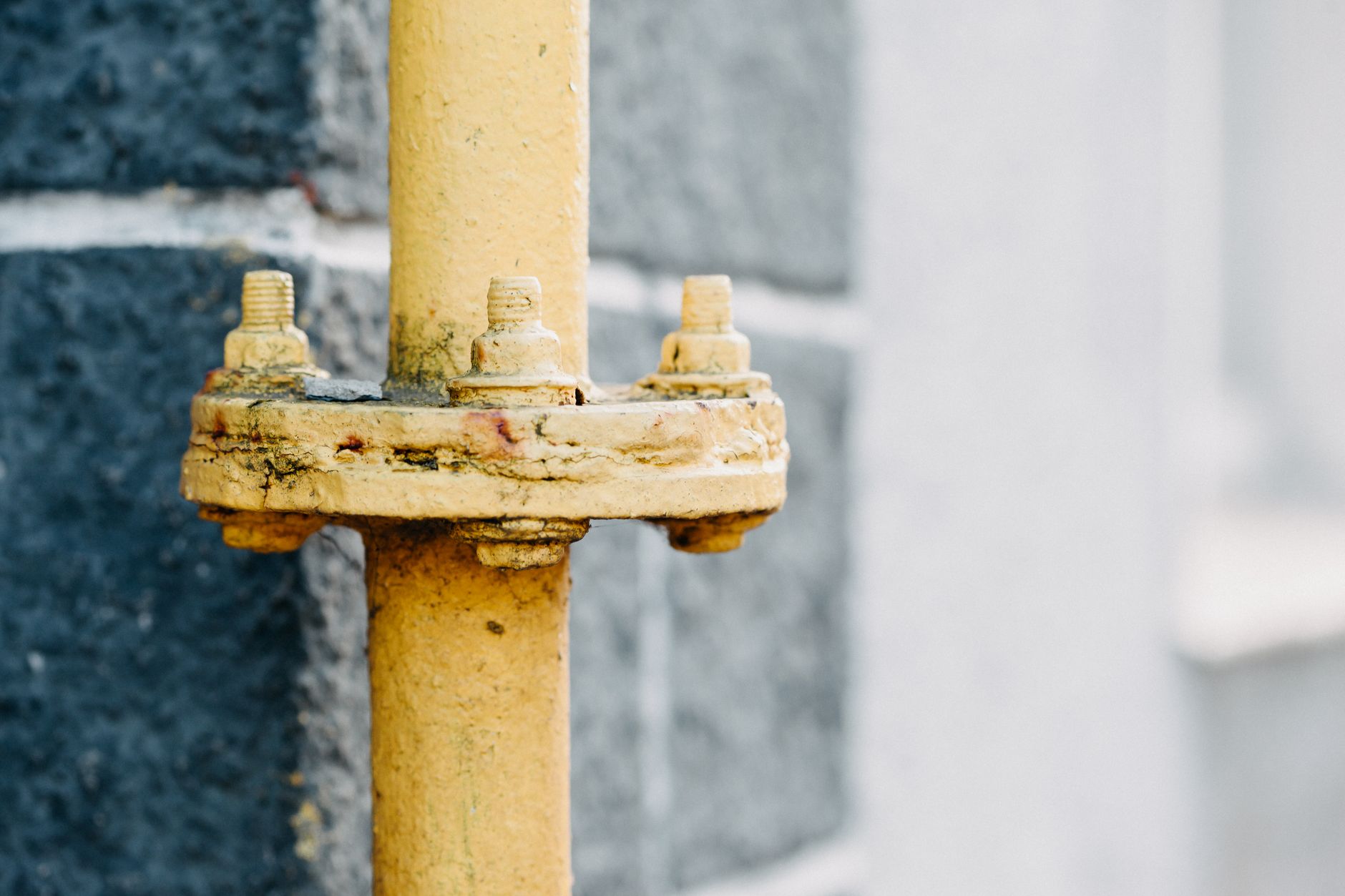 Detailed view of a rusty yellow gas pipe against a textured wall.