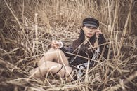 Woman with a Black Cap Sitting on Dry Grass