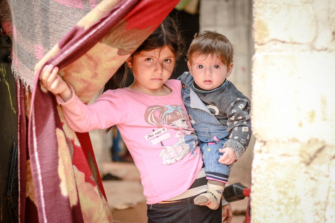 Free A young girl holding a baby stands in a doorway in Idlib, Syria, capturing resilience and innocence amidst conflict. Stock Photo