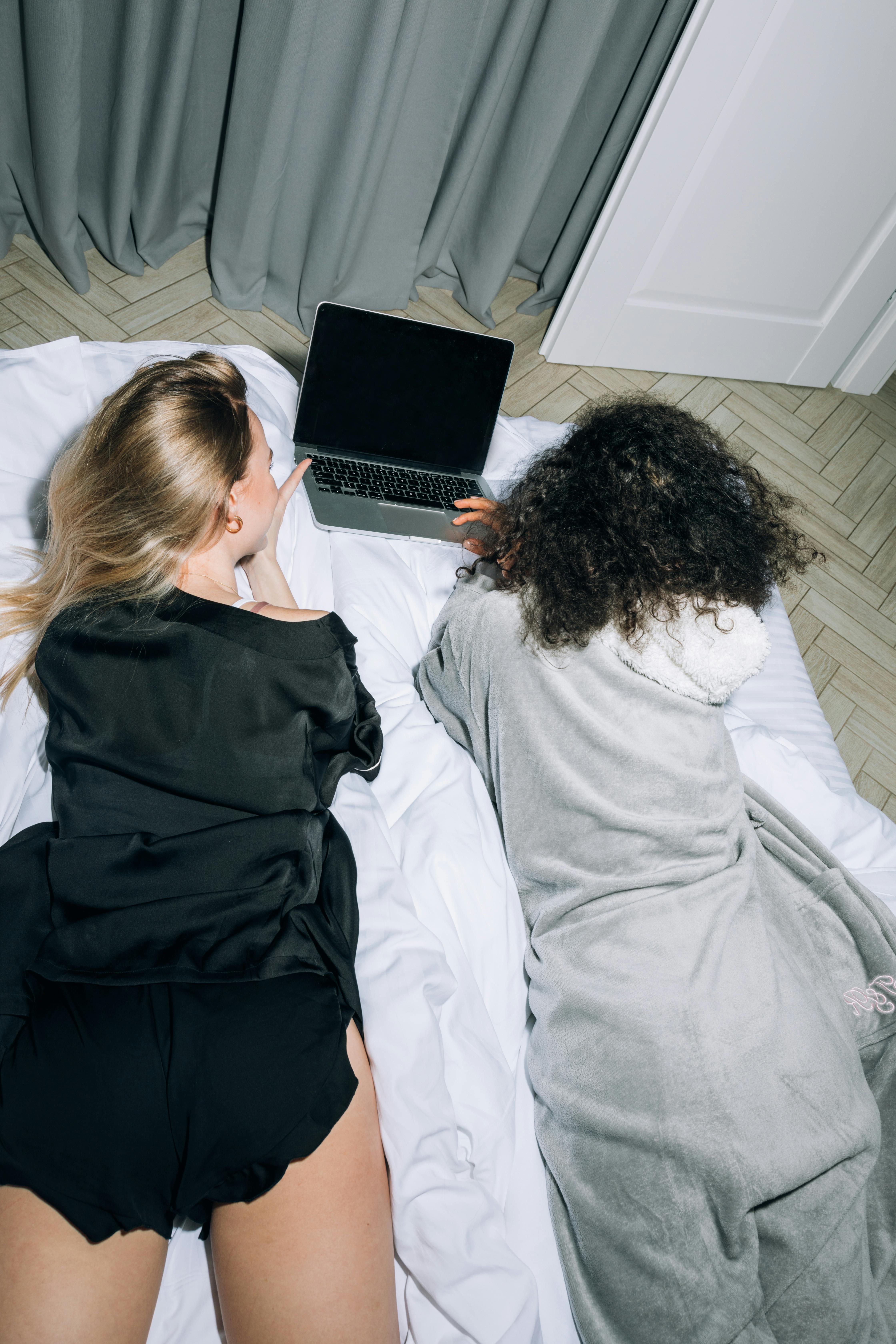 two young women lying down while looking at computer laptop