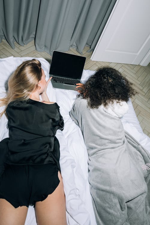 Two Young Women Lying Down While Looking at Computer Laptop