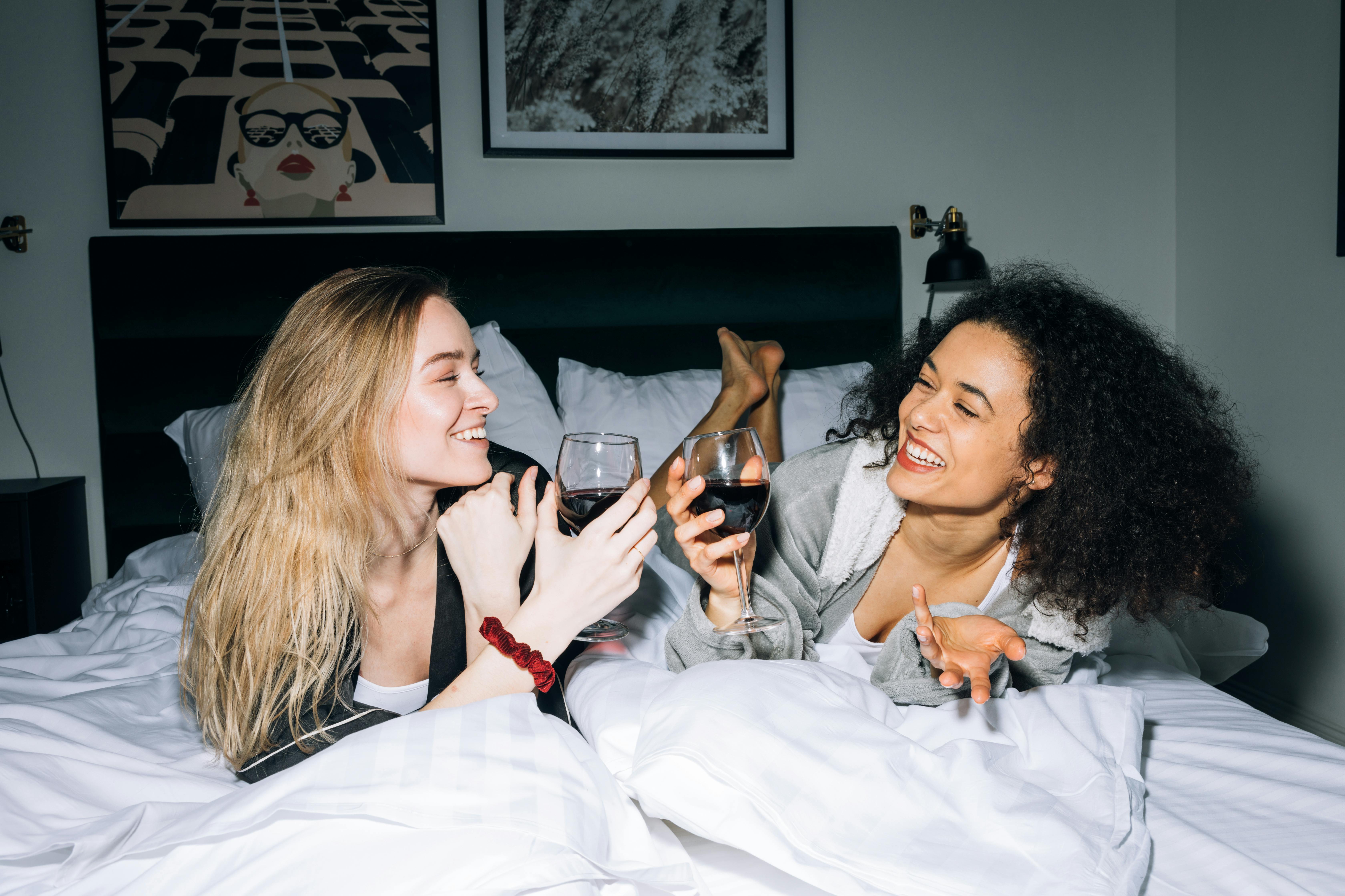 two young women lying on white bed while looking at each other